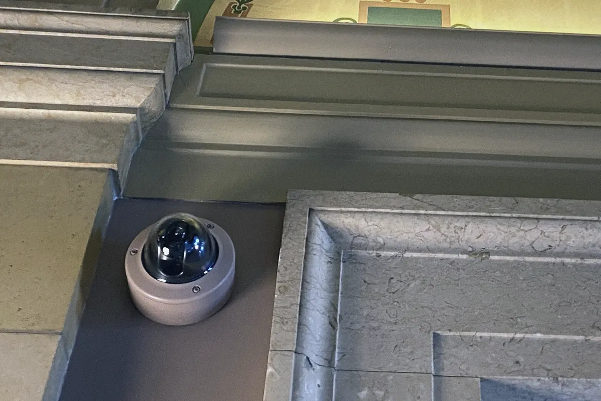 A white dome security camera mounted beneath ornate ceiling molding