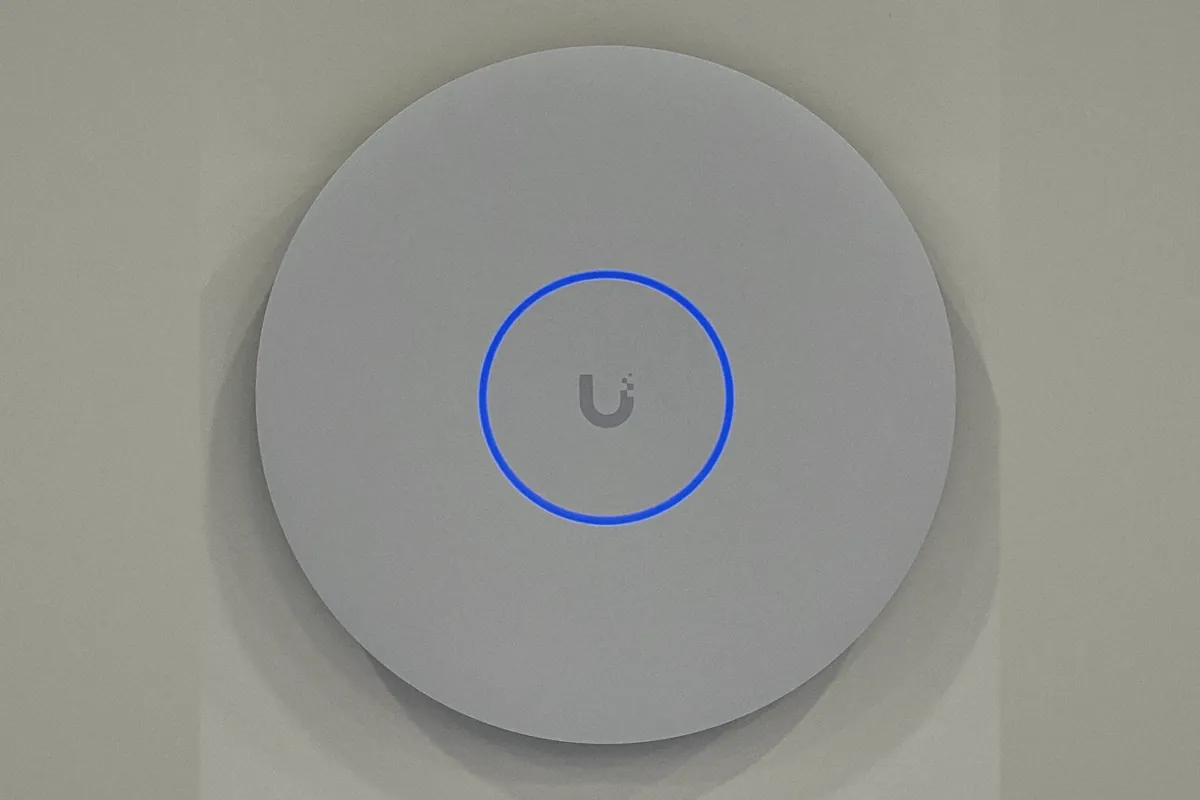 A UniFi U7 Pro XGS Wi-Fi 7 access point, a slim white disc with a soft blue ring light
